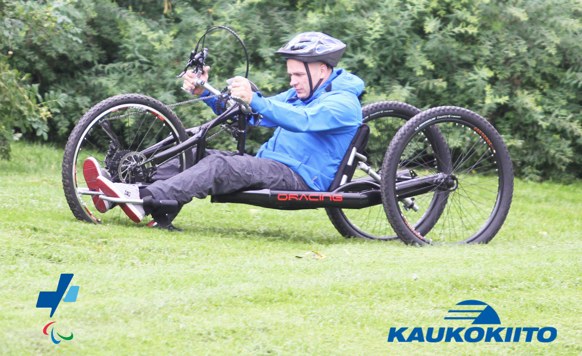 Henkilö polkemassa käsipyörällä nurmikolla. Kuvan päällä Kaukokiidon ja Suomen Paralympiakomitean logot.