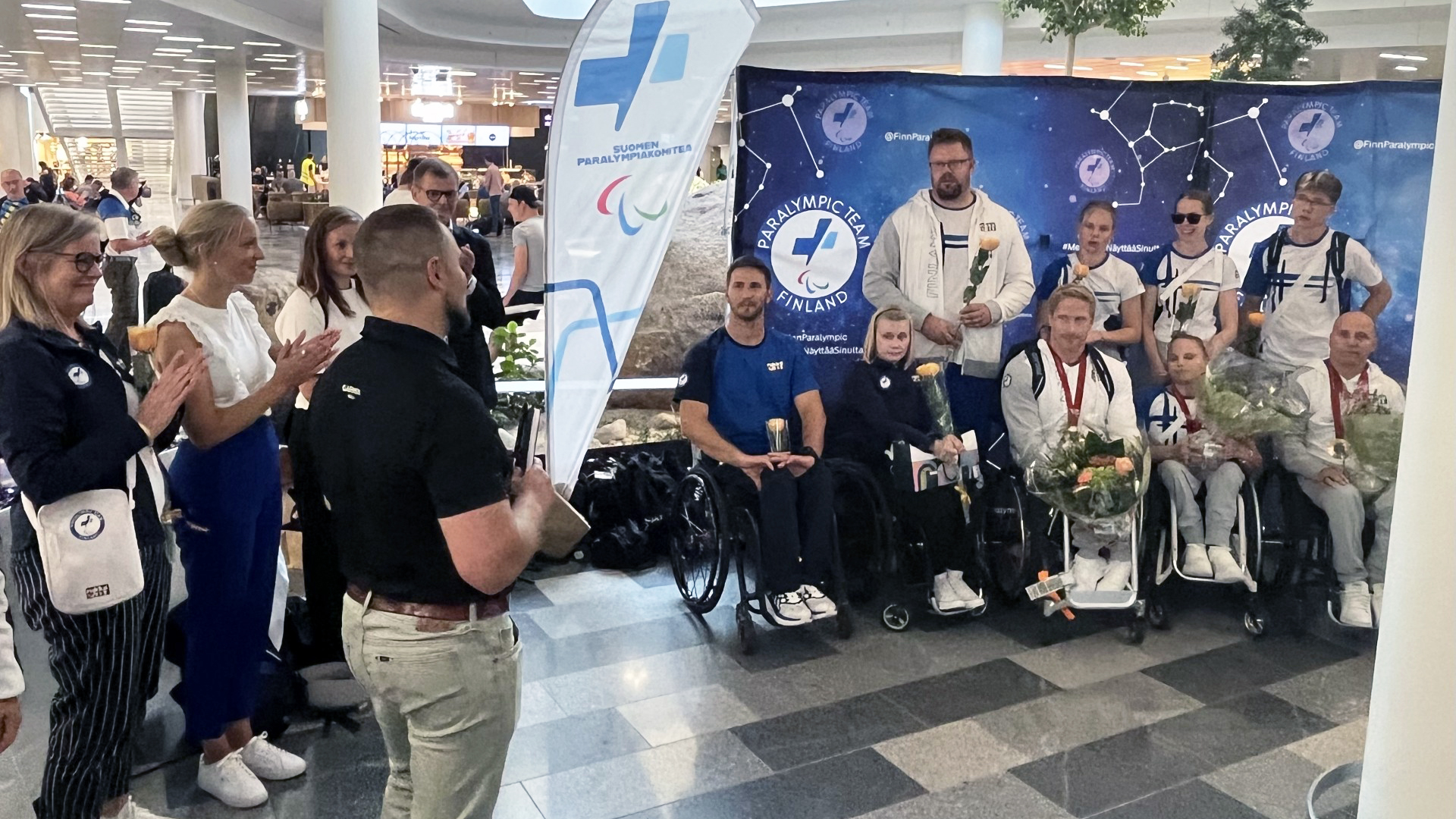 Paralympiajoukkueen urheilijoita lentokentällä yhteiskuvassa kukitettuina.